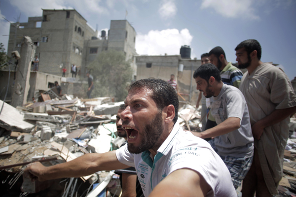 Palestinians watch as others carry a body from the rubble of a house destroyed by an Israeli missile strike in Gaza City, July 21, 2014. AP photo