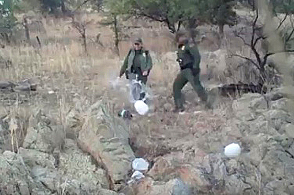 Border Patrol Agents kick over plastic jugs of water.